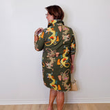 Woman wearing a patterned dress with dragons against a white wall.