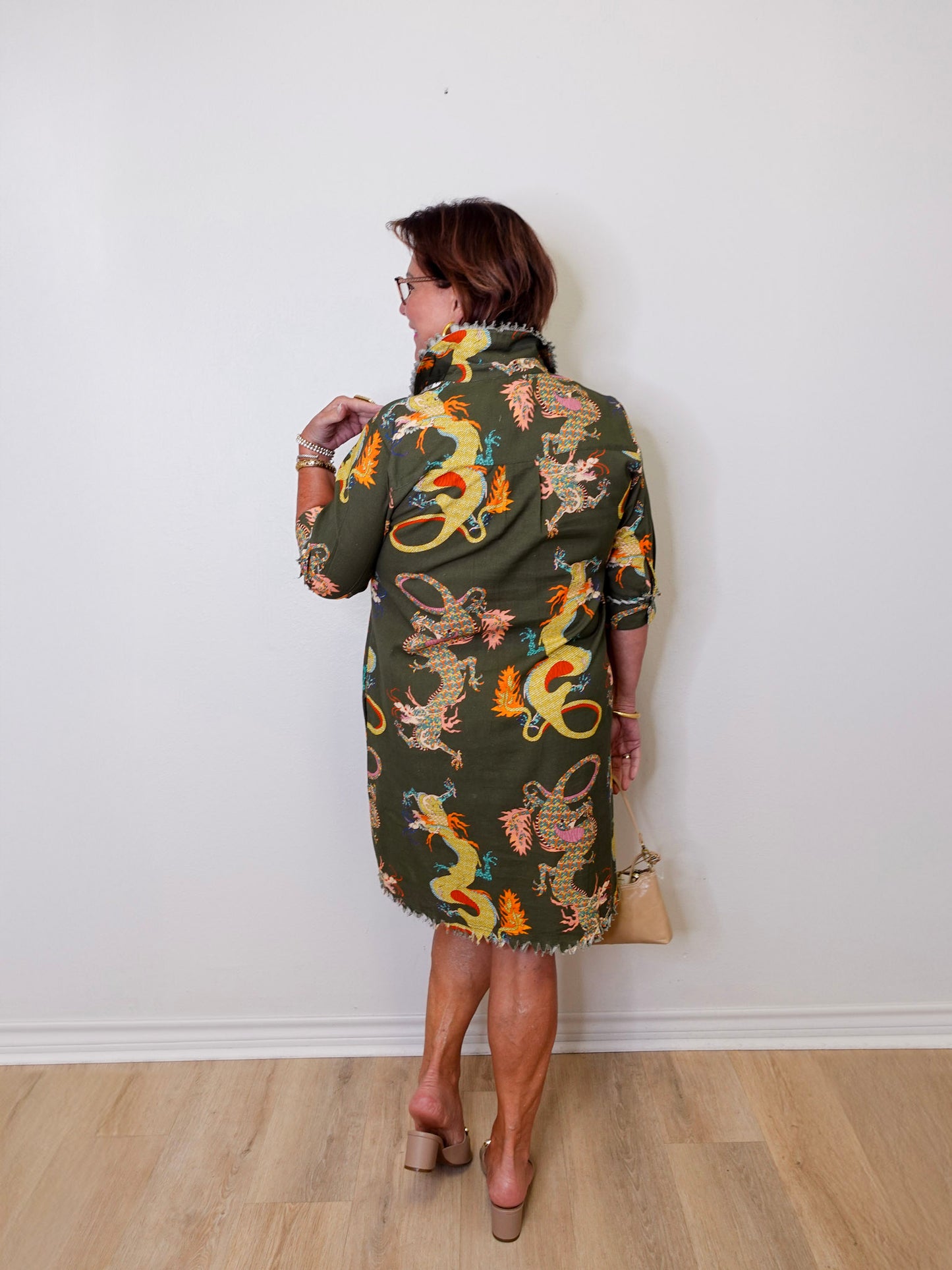 Woman wearing a patterned dress with dragons against a white wall.
