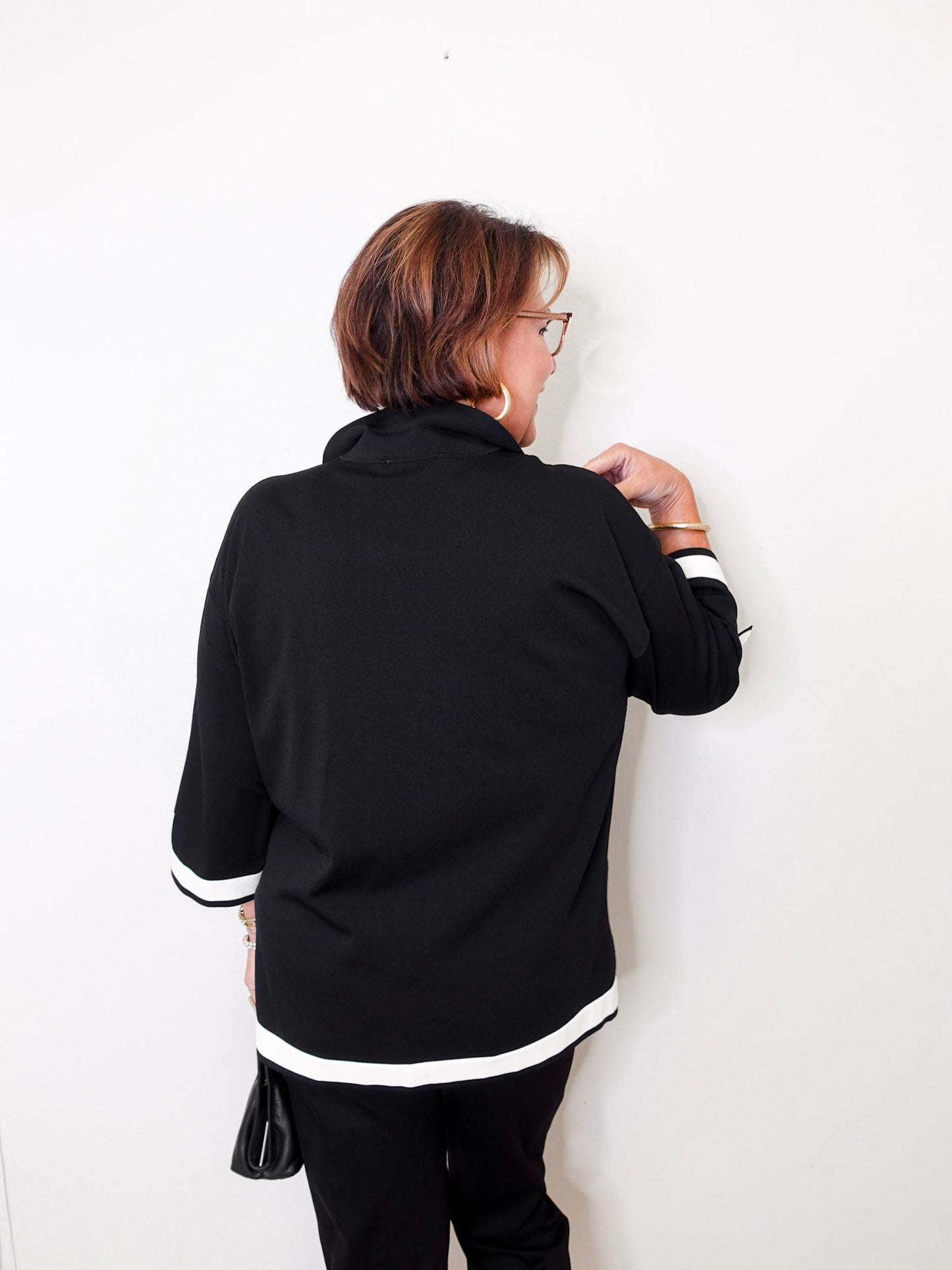 Person wearing a black jacket with white trim against a white wall