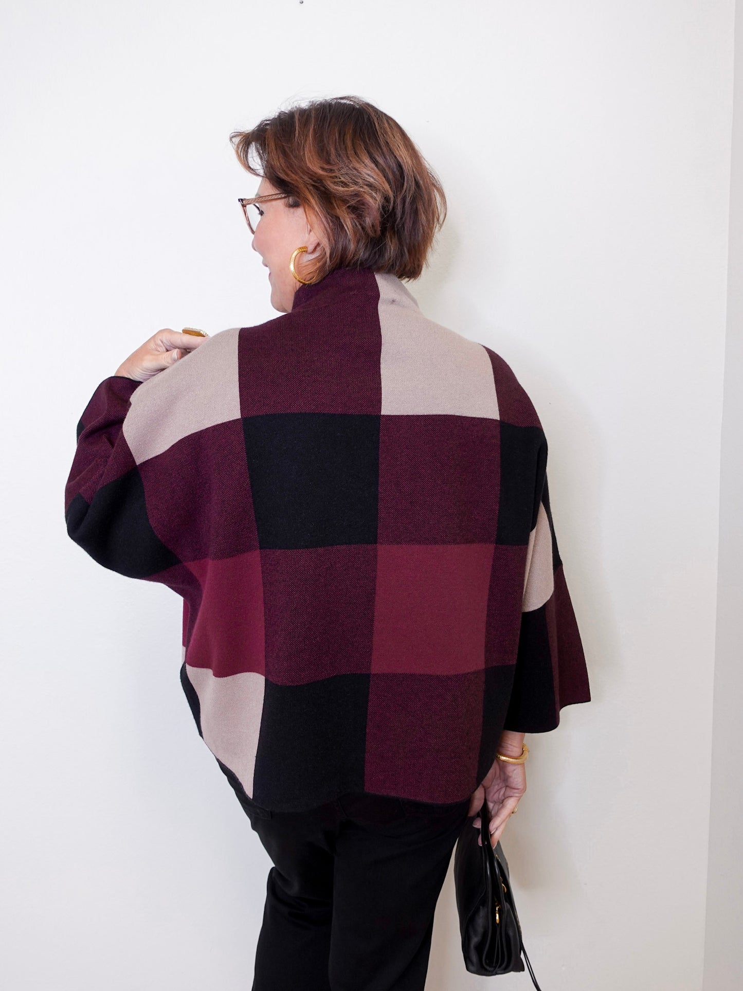 Person wearing a plaid poncho against a white wall
