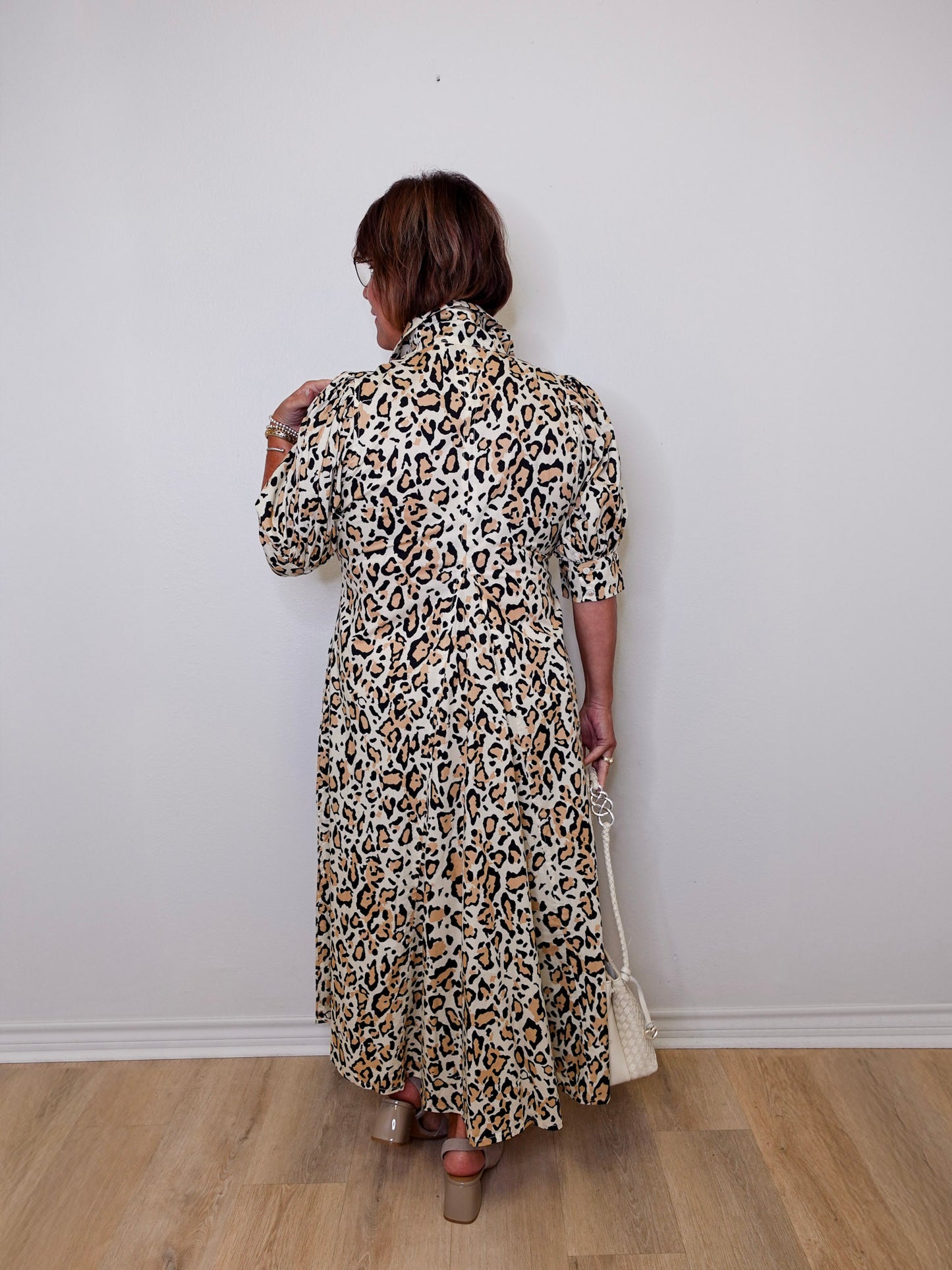 Person wearing a leopard print dress against a white wall.