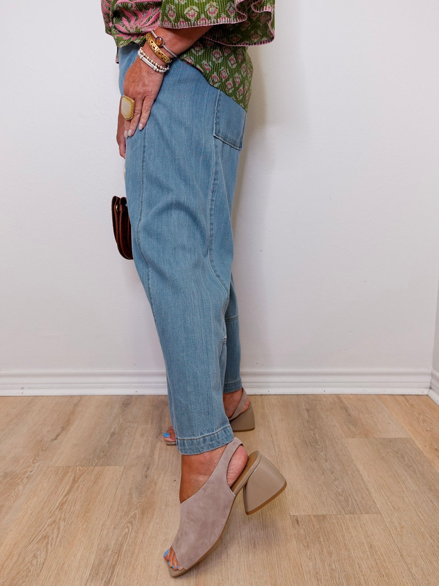 Person wearing blue jeans and beige sandals on a wooden floor.
