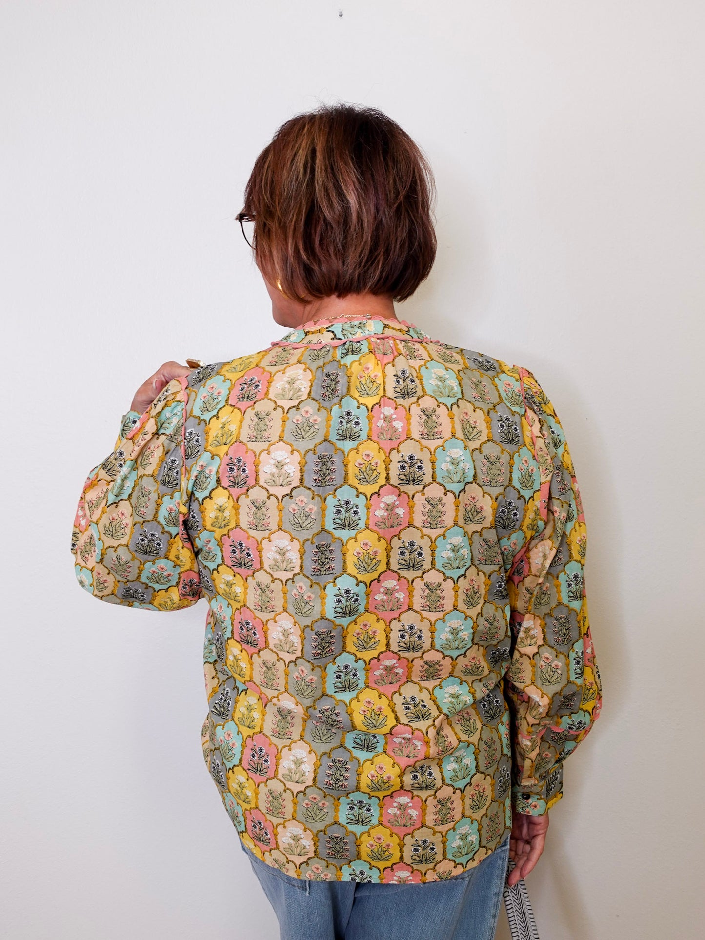 Person wearing a patterned blouse against a white wall