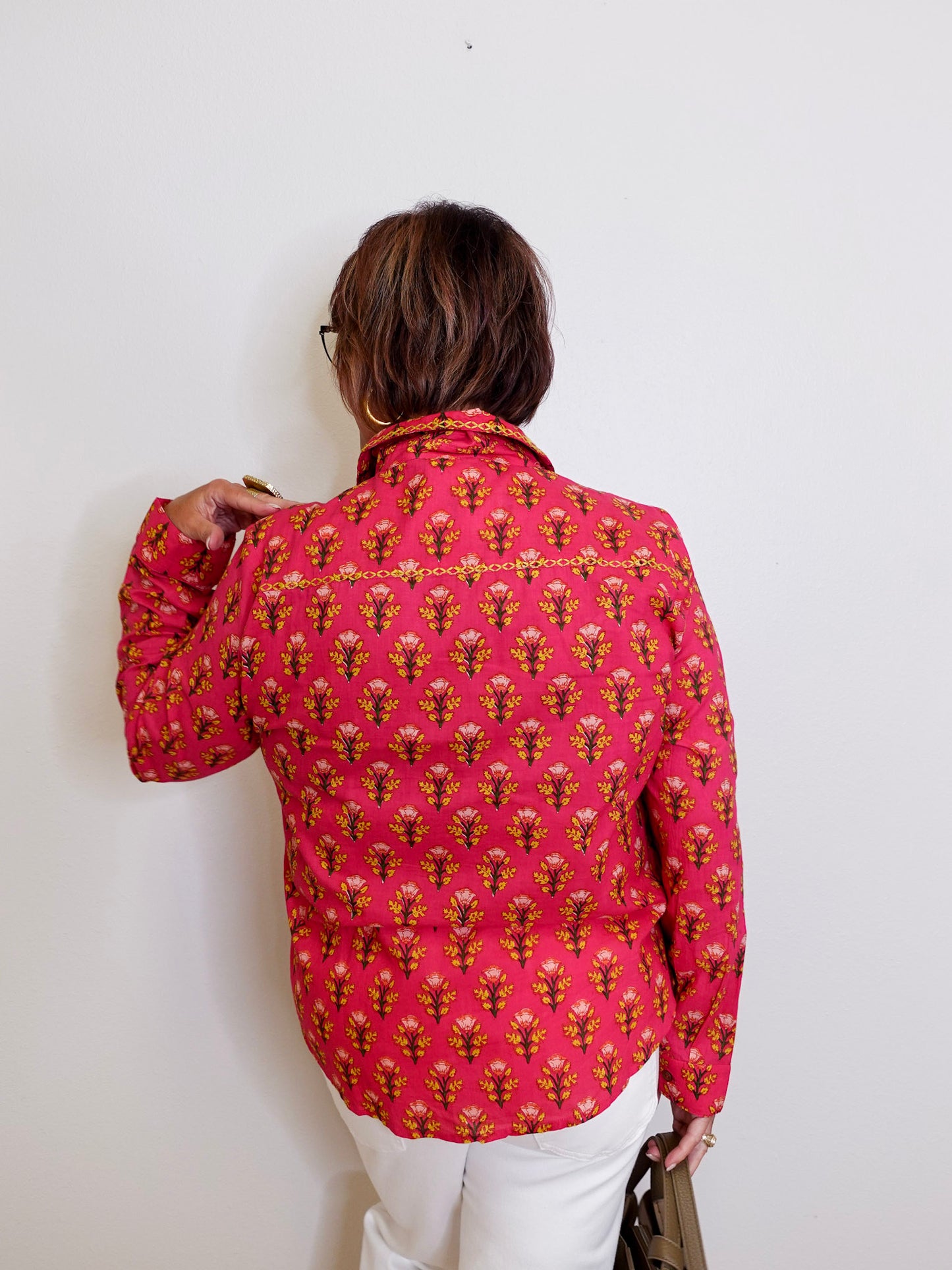 Person wearing a pink patterned shirt against a white wall