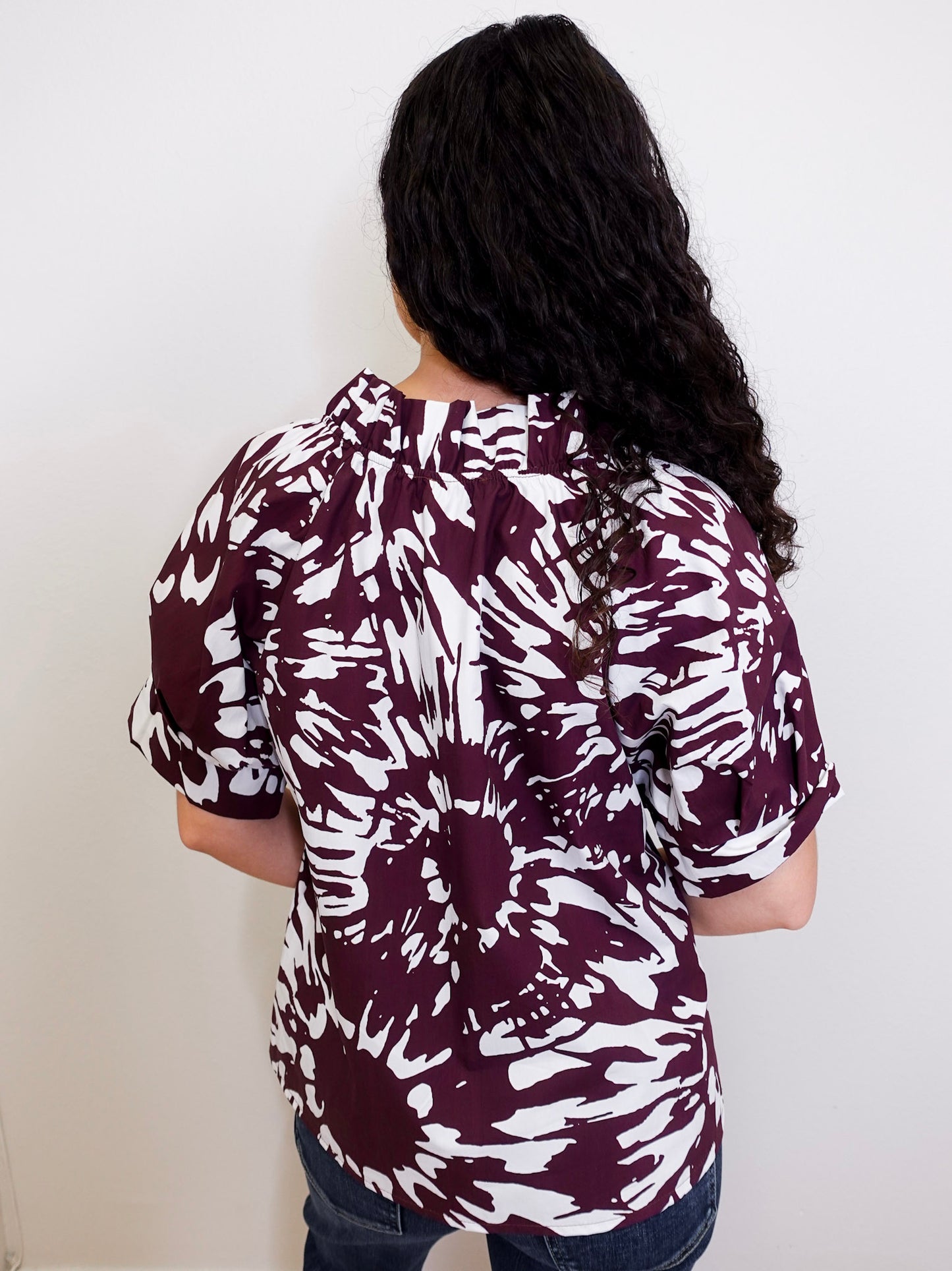 Person wearing a maroon and white patterned shirt against a plain background
