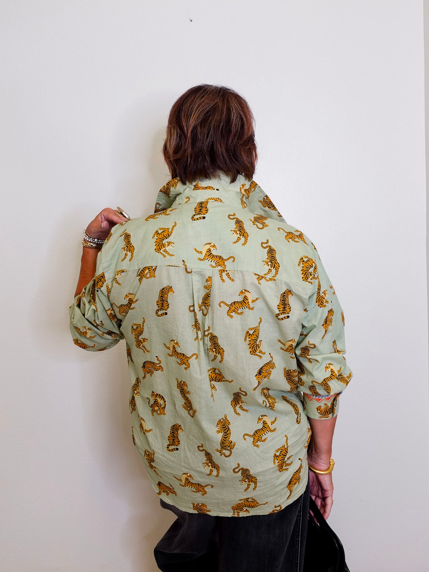 Person wearing a light green shirt with gold tiger patterns against a white background
