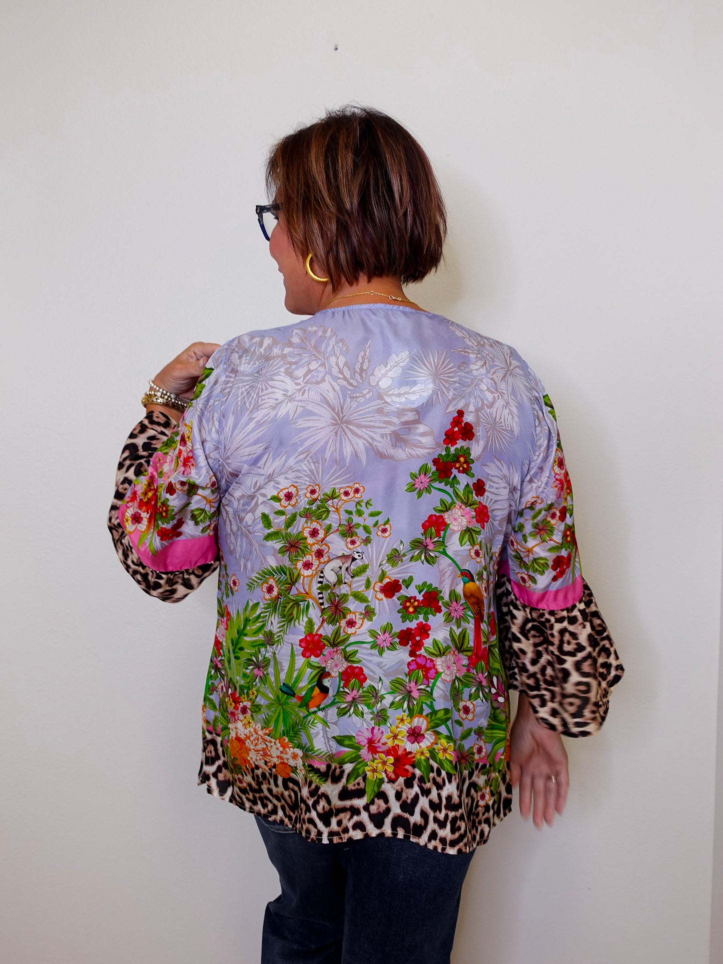 Person wearing a colorful floral and leopard print jacket against a white wall