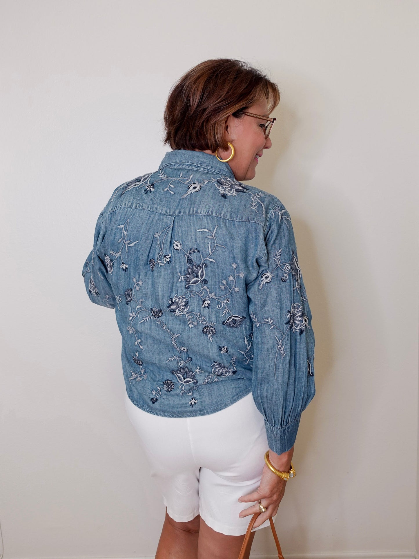 Person wearing a blue embroidered denim jacket and white shorts against a plain background