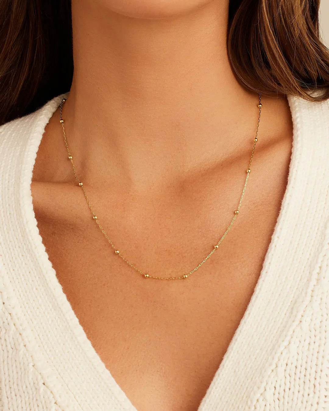 Gold necklace on a person wearing a white sweater