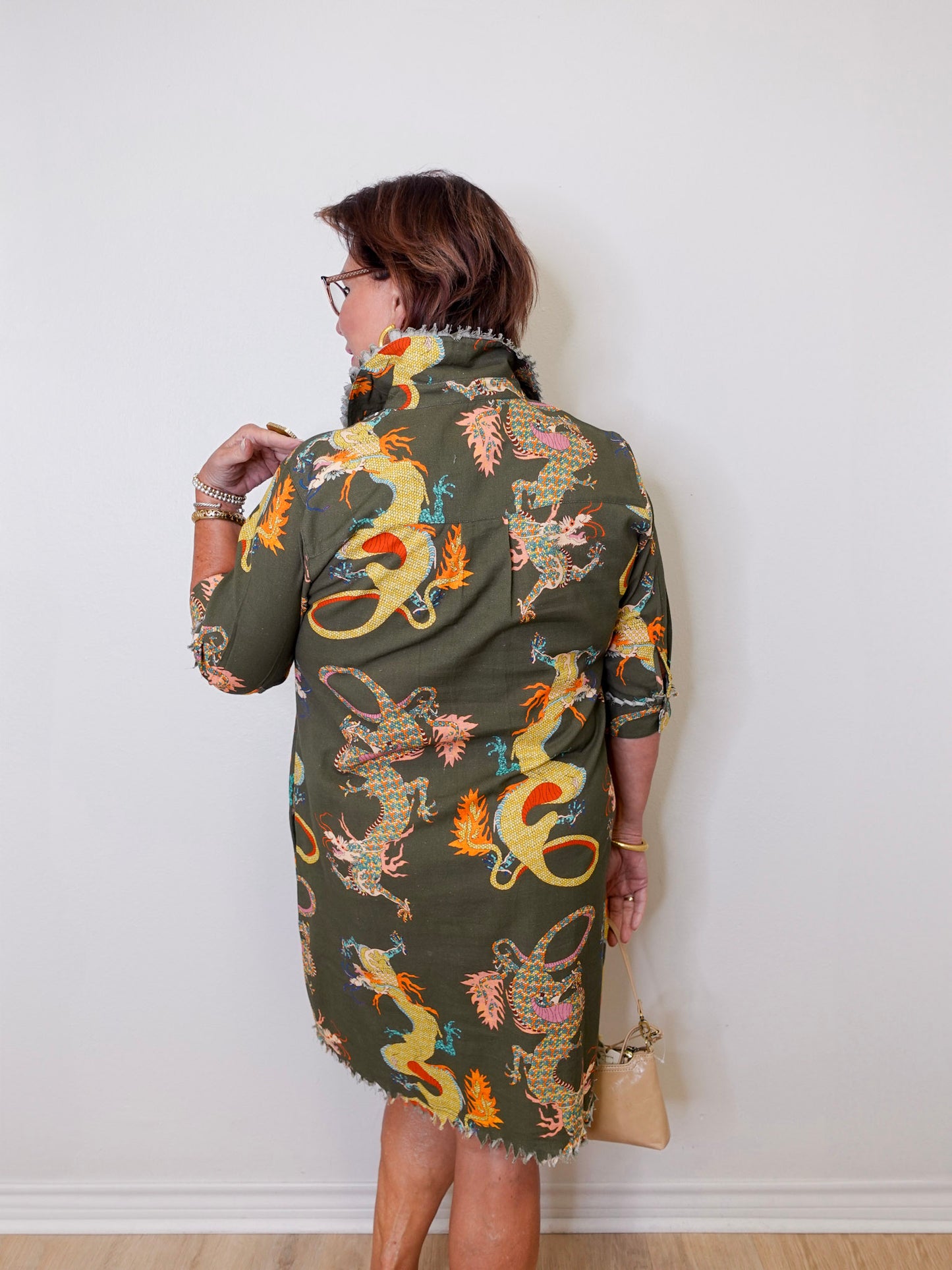 Woman wearing a green dress with dragon pattern against a white wall