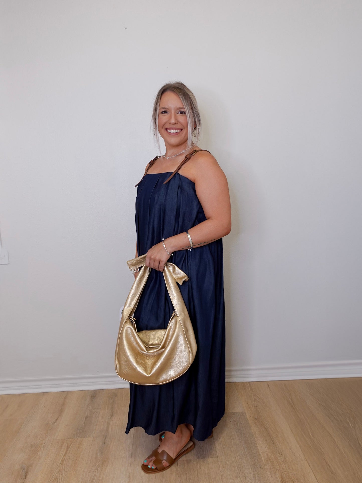 Woman in a navy dress holding a gold handbag against a white wall.