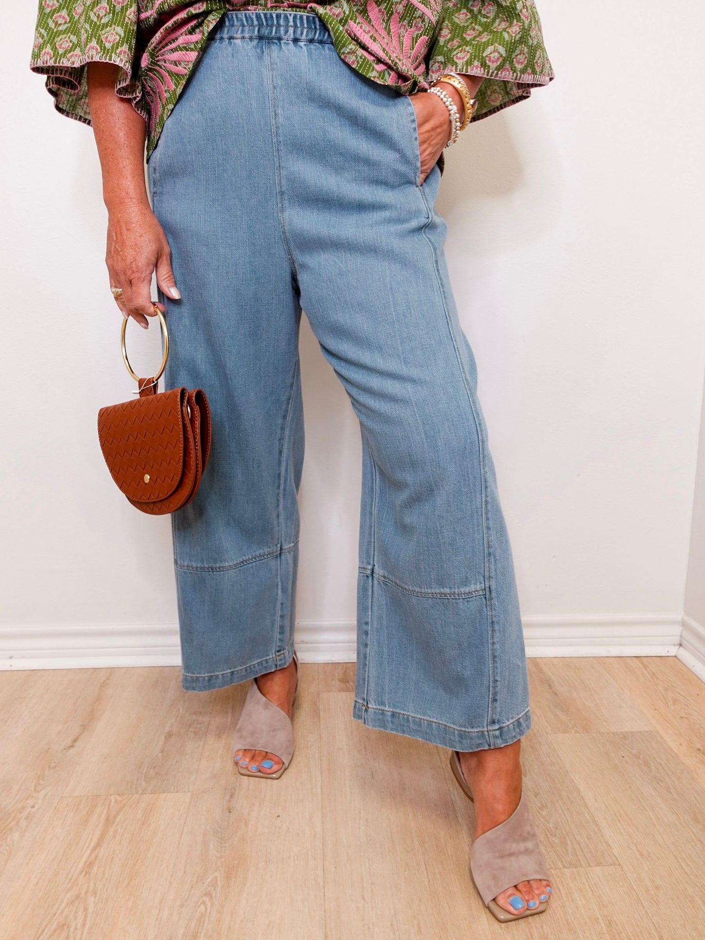 Person wearing blue jeans and holding a brown handbag against a white wall.