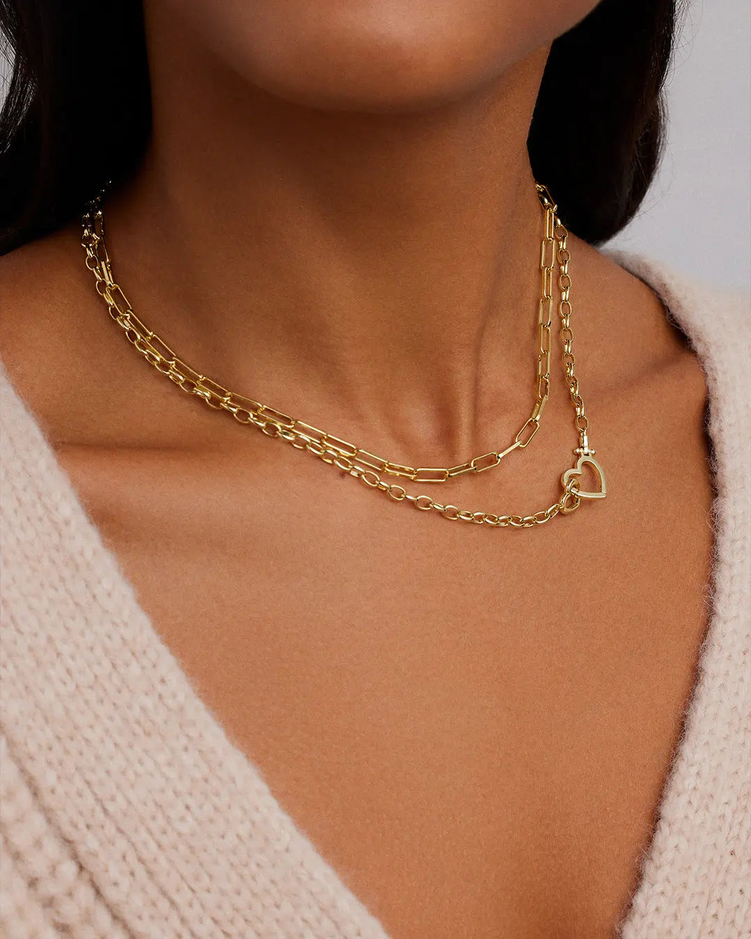Gold chain necklace with a heart pendant on a person wearing a beige sweater.