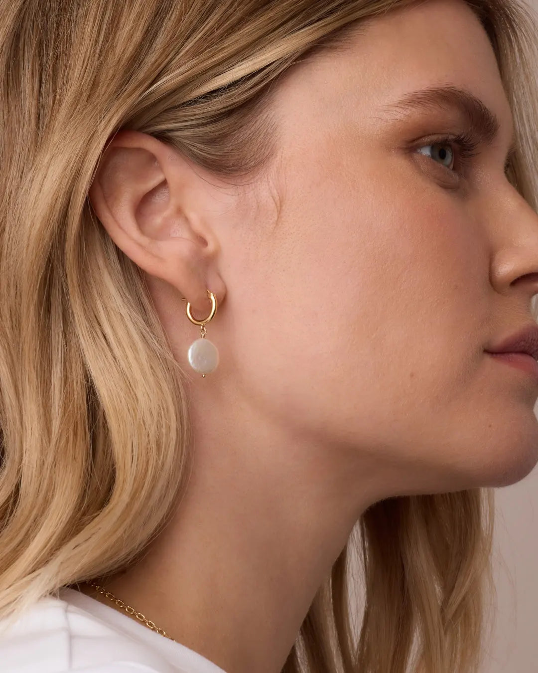 Close-up of a woman wearing gold hoop earrings with a neutral background