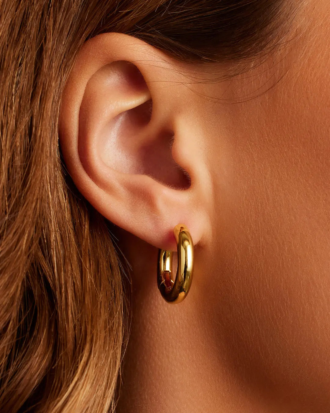 Close-up of an ear wearing a gold hoop earring with a blurred background