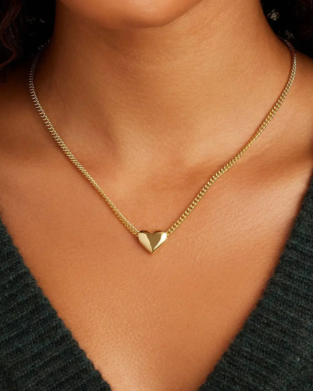 Gold heart necklace on a person wearing a dark green top