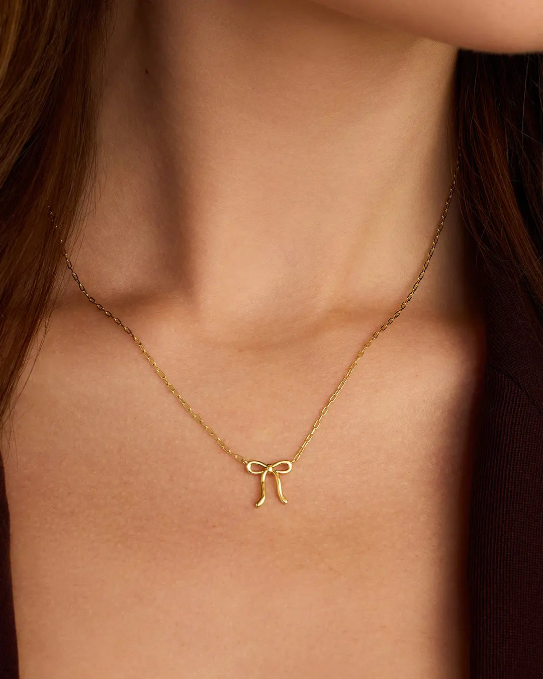 Gold necklace with a bow pendant on a person's neck