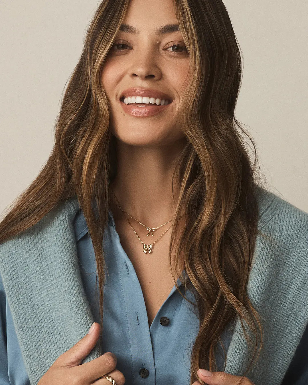 Woman wearing a light blue vest over a blue shirt with a neutral background