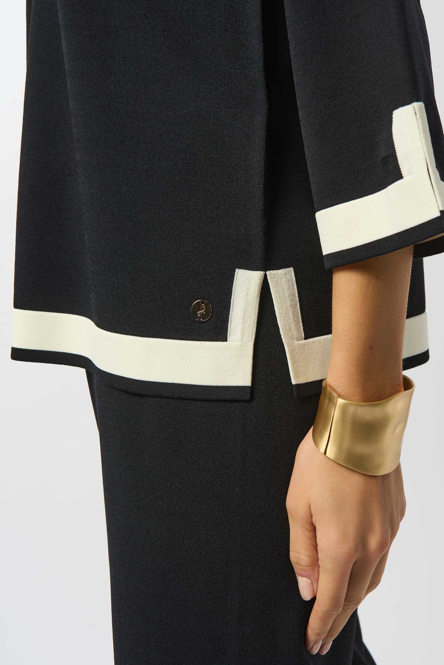 Black outfit with white trim and gold cuff on a plain background