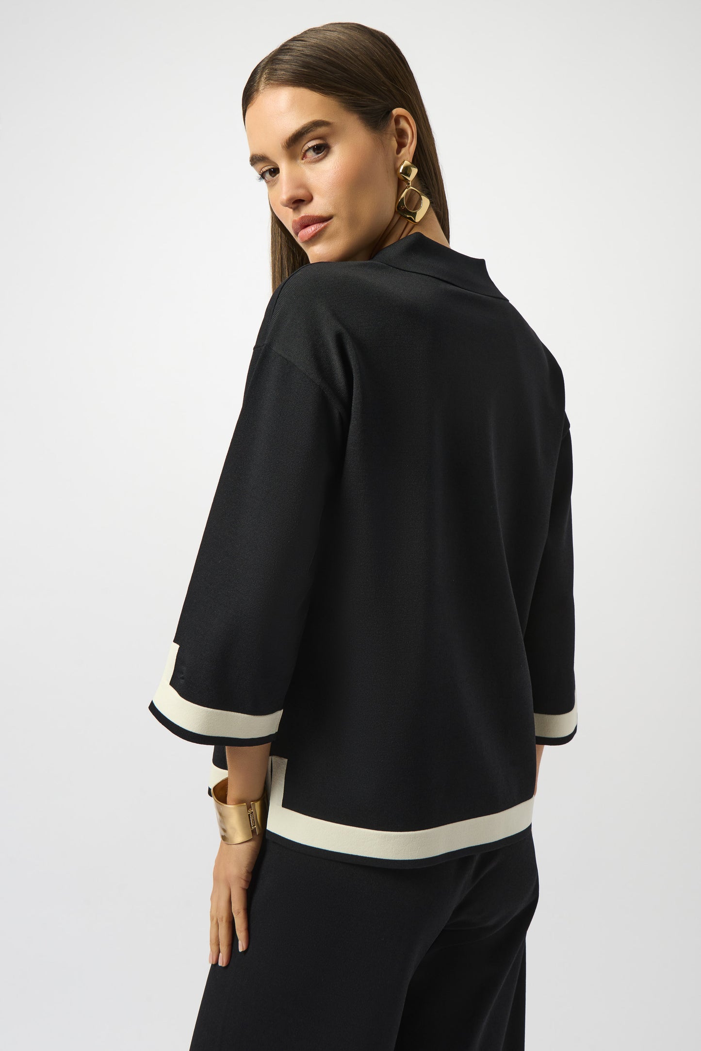 Woman wearing a black outfit with white trim on a plain background