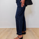 Person wearing dark blue jeans and a black outfit against a white wall.