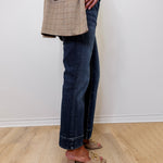 Person wearing a plaid blazer, dark jeans, and beige shoes on a light wooden floor.