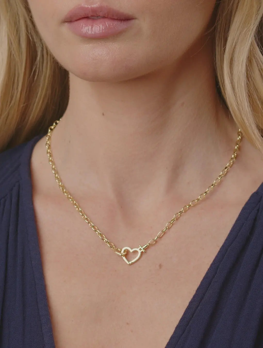 Gold necklace with a heart pendant worn by a person against a neutral background