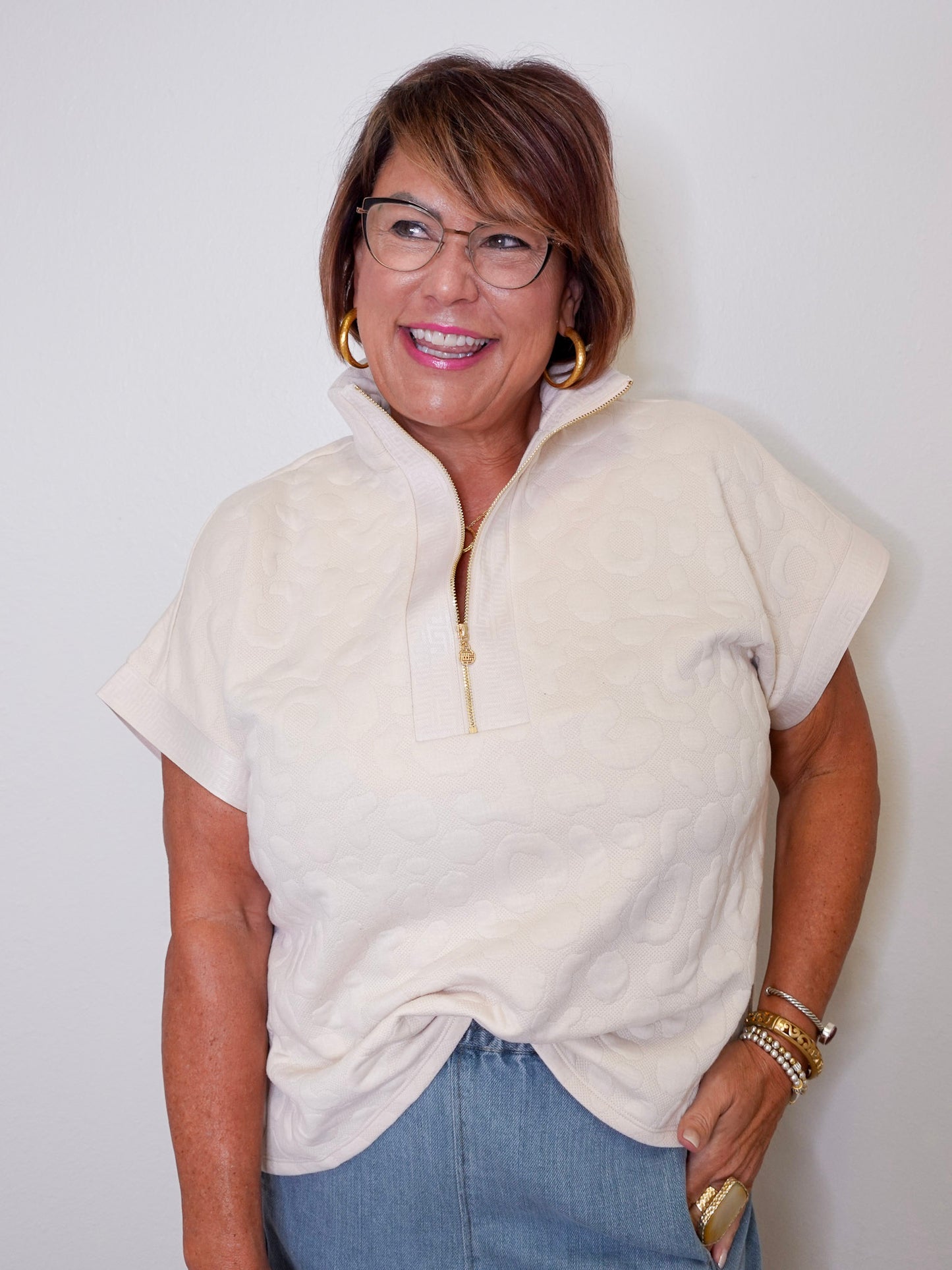 Woman wearing a cream-colored zip-up sweater and blue jeans against a white background