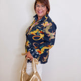 Woman wearing a colorful dragon patterned jacket holding a gold handbag against a white wall.