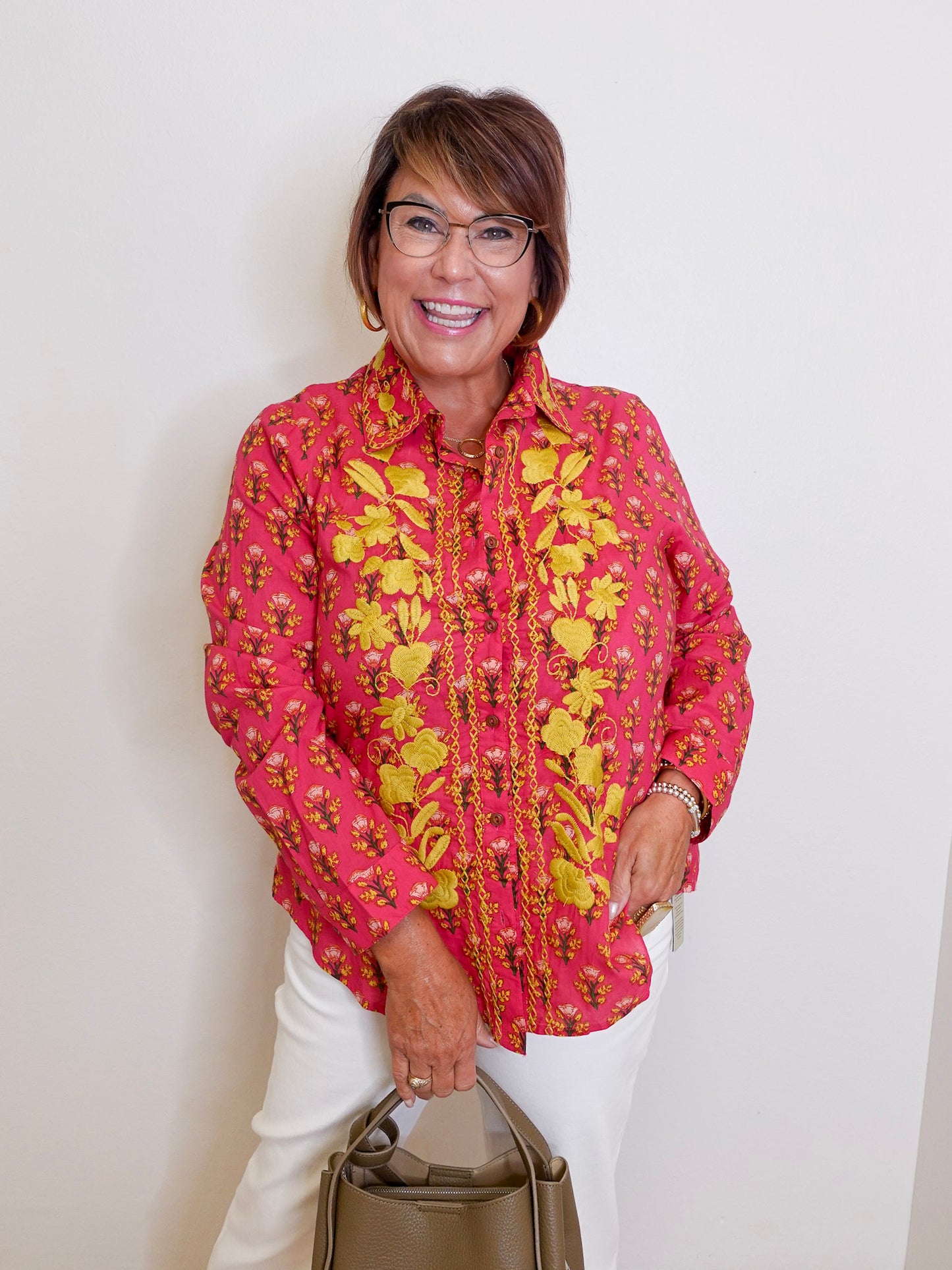 Woman wearing a pink floral blouse with a beige handbag against a white background