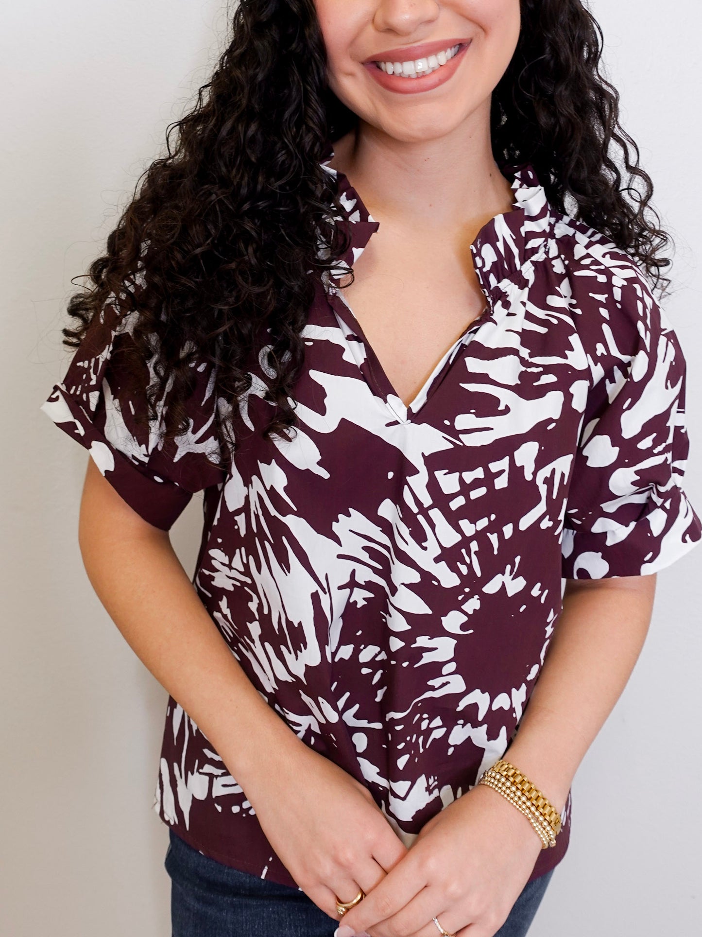 Woman wearing a maroon and white patterned blouse against a plain background