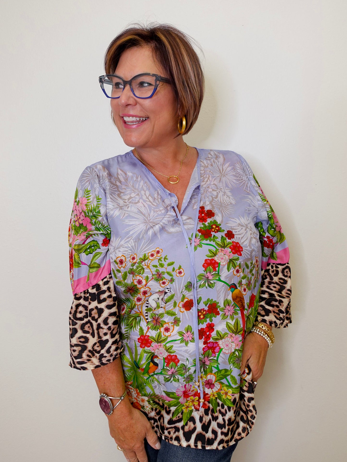 Woman wearing a colorful floral blouse with leopard print sleeves against a white background