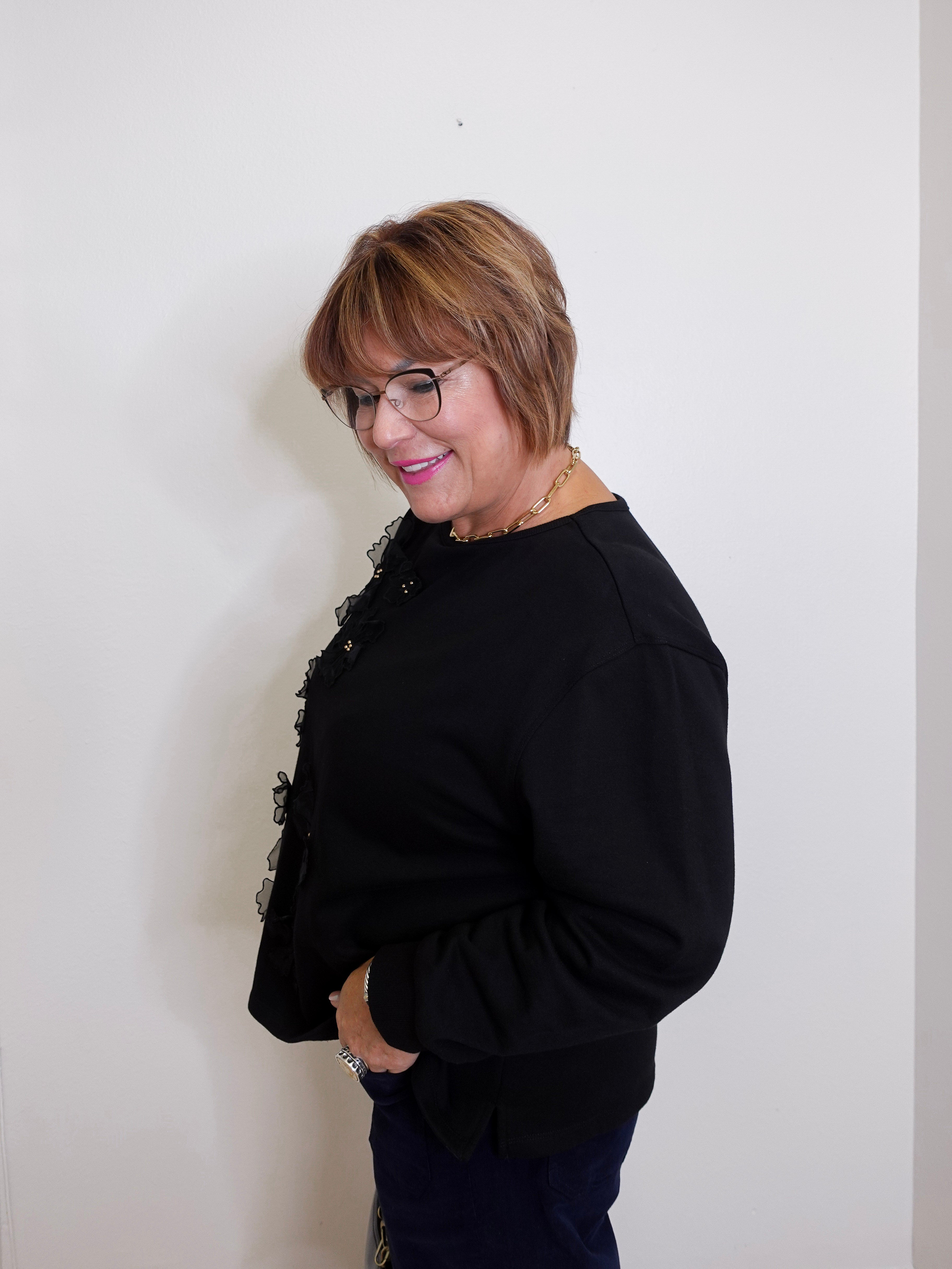 Woman wearing a black outfit with floral details against a plain background