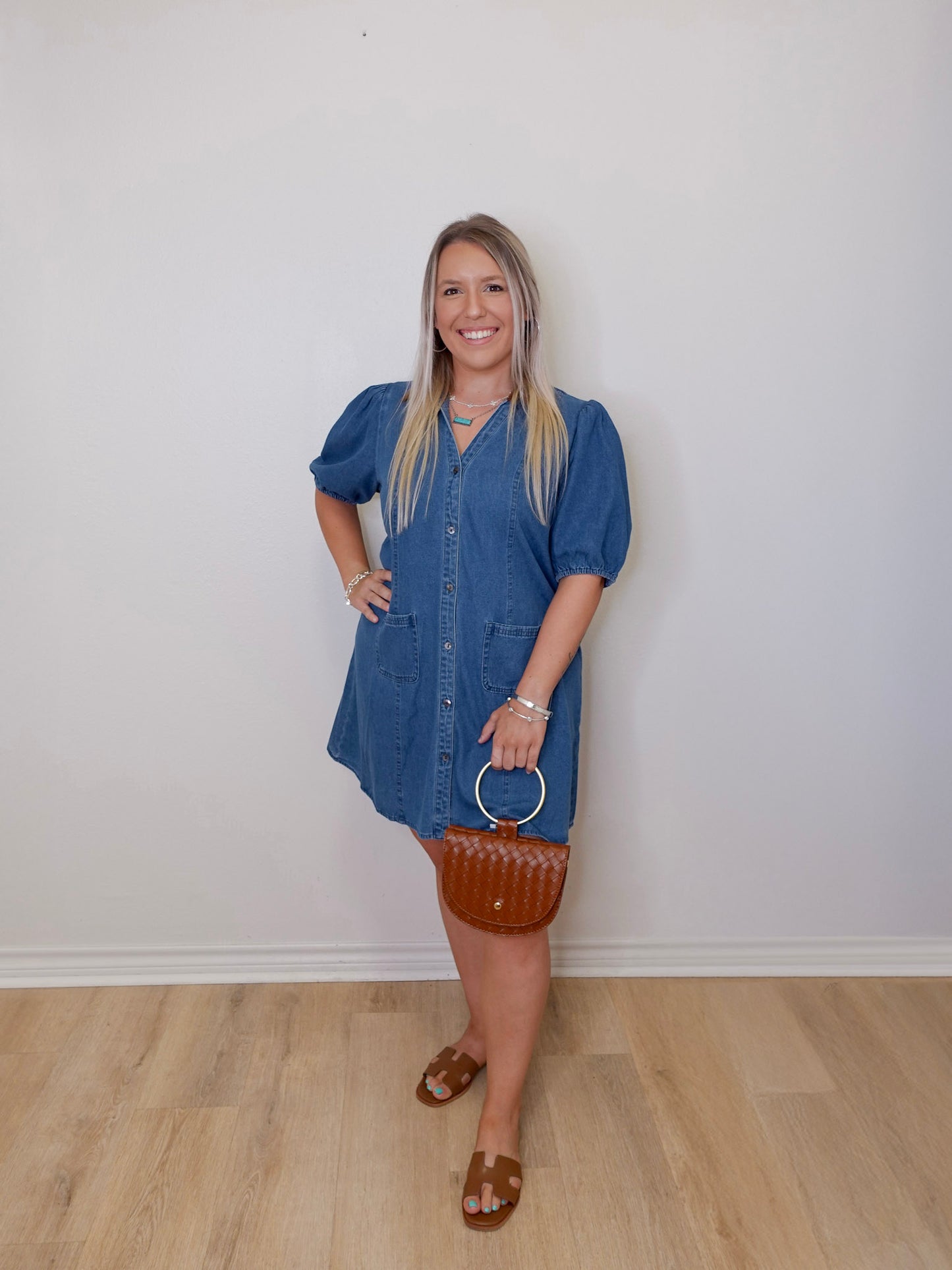 Woman wearing a blue dress standing against a white wall.