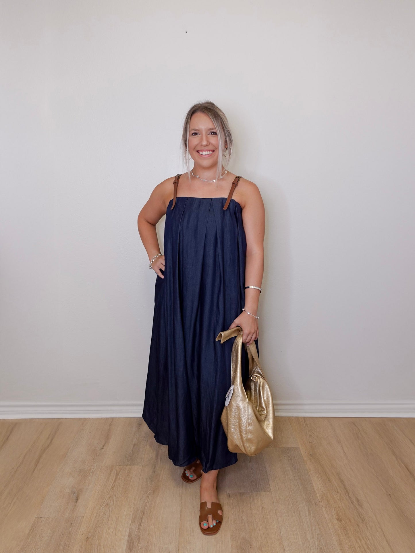 Woman in a navy dress holding a gold handbag against a white wall.