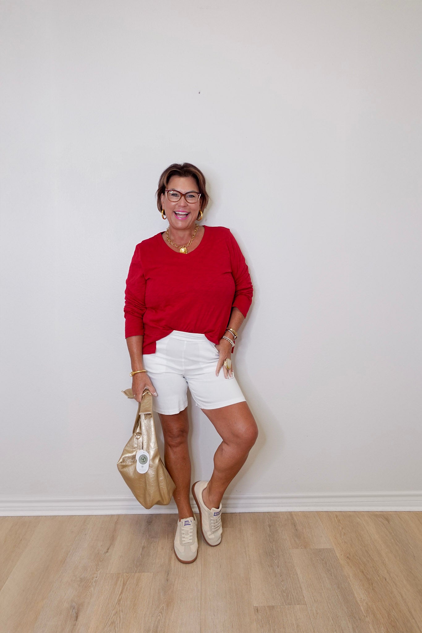 Woman in a red top and white shorts posing against a plain wall.