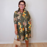 Woman wearing a patterned dress with dragons, holding a beige handbag indoors.