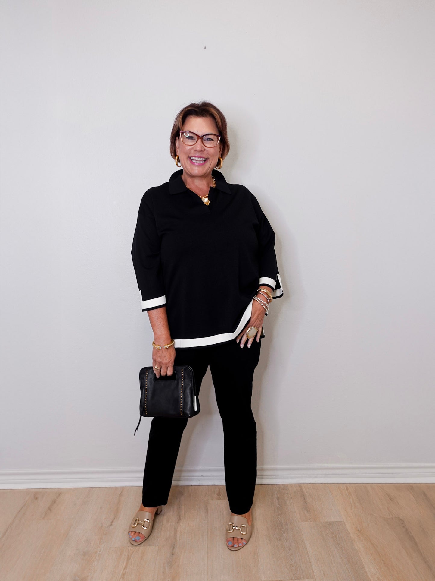 Woman wearing a black outfit with white trim against a plain wall.
