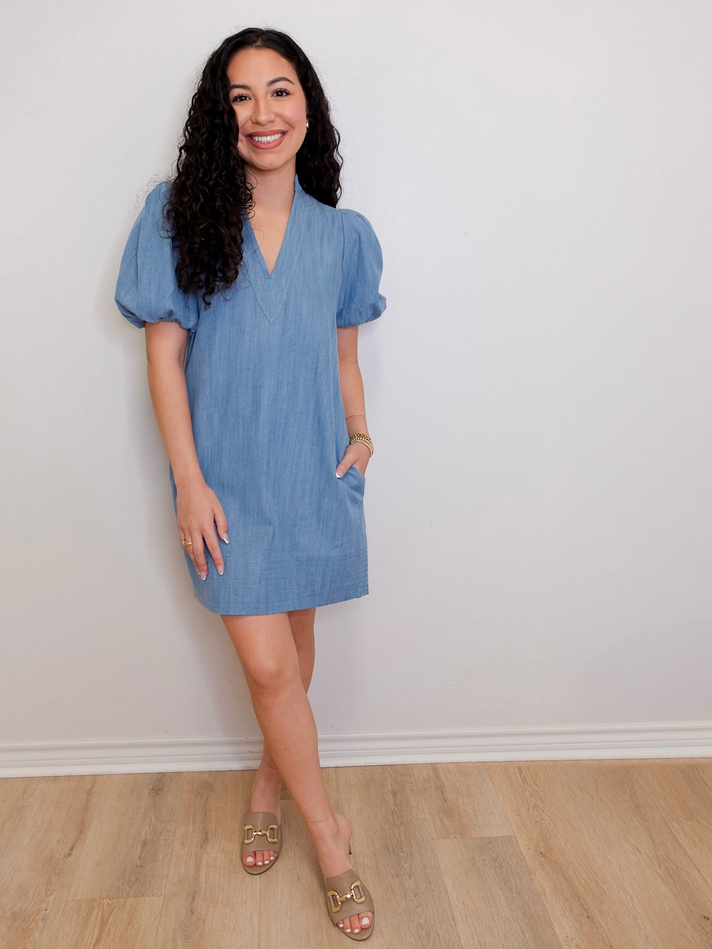 Woman wearing a blue dress standing against a white wall.