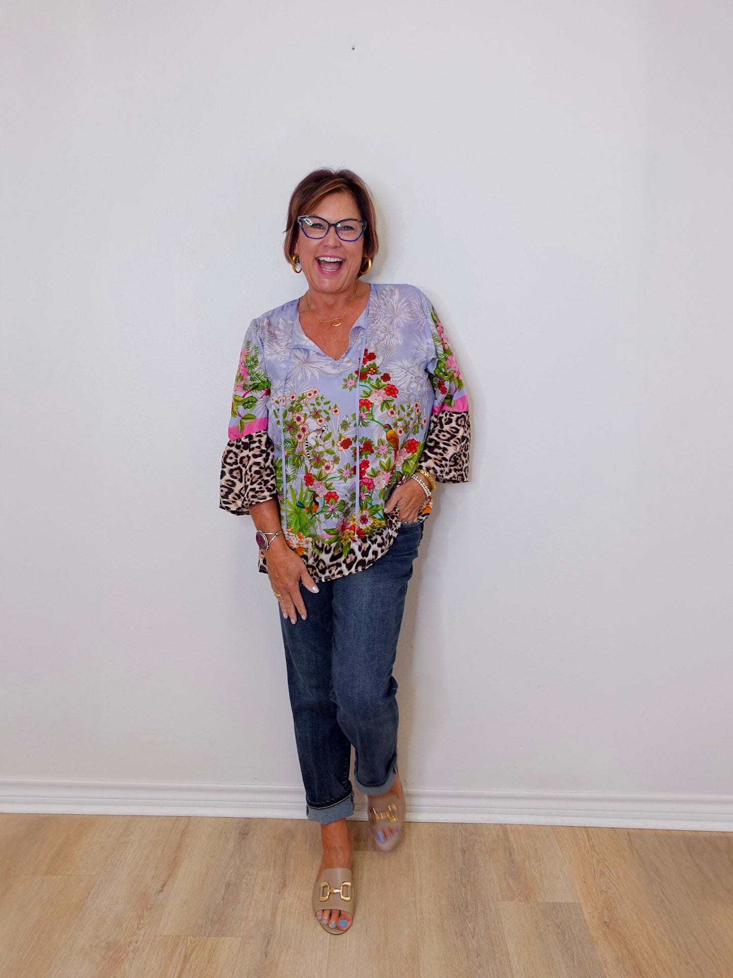Woman wearing a colorful floral blouse with leopard print accents and blue jeans against a white wall.