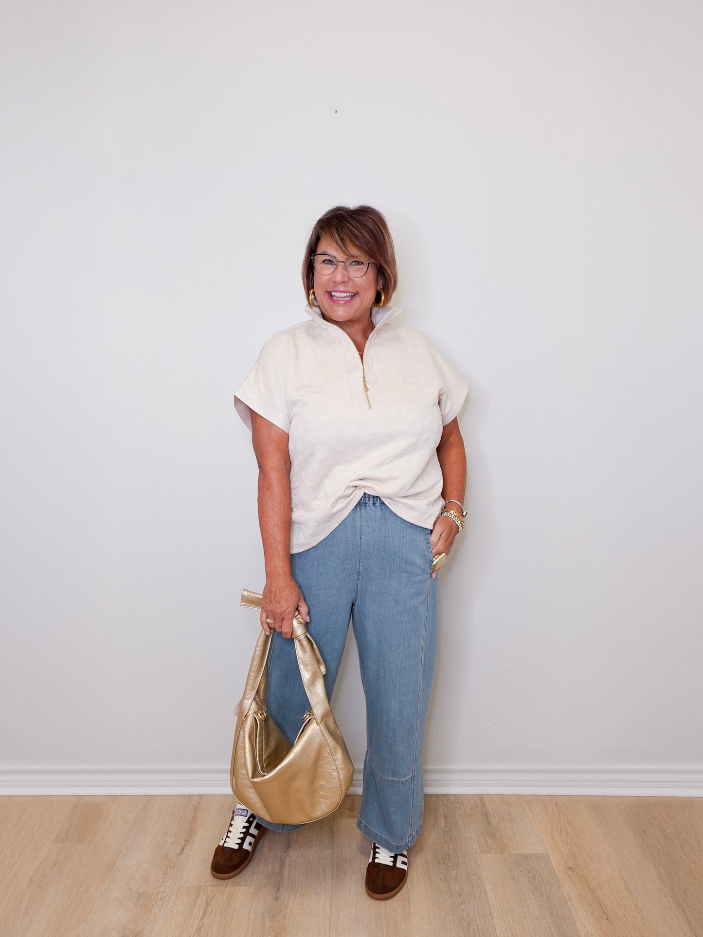 Woman holding a gold handbag against a white wall