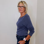 Woman wearing a blue top and dark jeans against a white wall