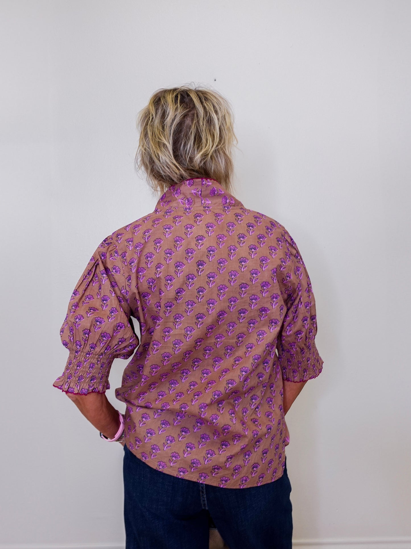 Person wearing a patterned shirt with their back to the camera against a plain background