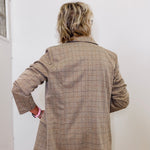 Person wearing a beige checkered blazer against a white wall