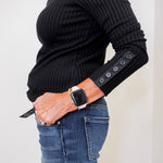 Person wearing a black ribbed sweater with button details on the sleeves, paired with blue jeans.