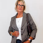 Woman wearing a brown  blazer, white shirt, and jeans with a handbag against a plain background