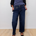 Person wearing dark blue jeans and a black top against a white wall.