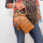 Person holding a brown woven handbag with a patterned top and jeans.