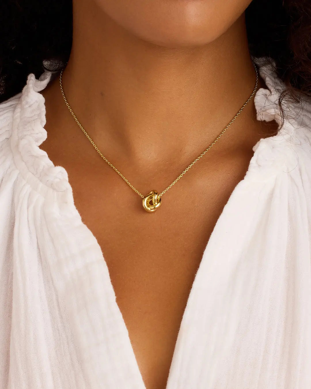 Gold necklace with a pendant worn by a person in a white blouse