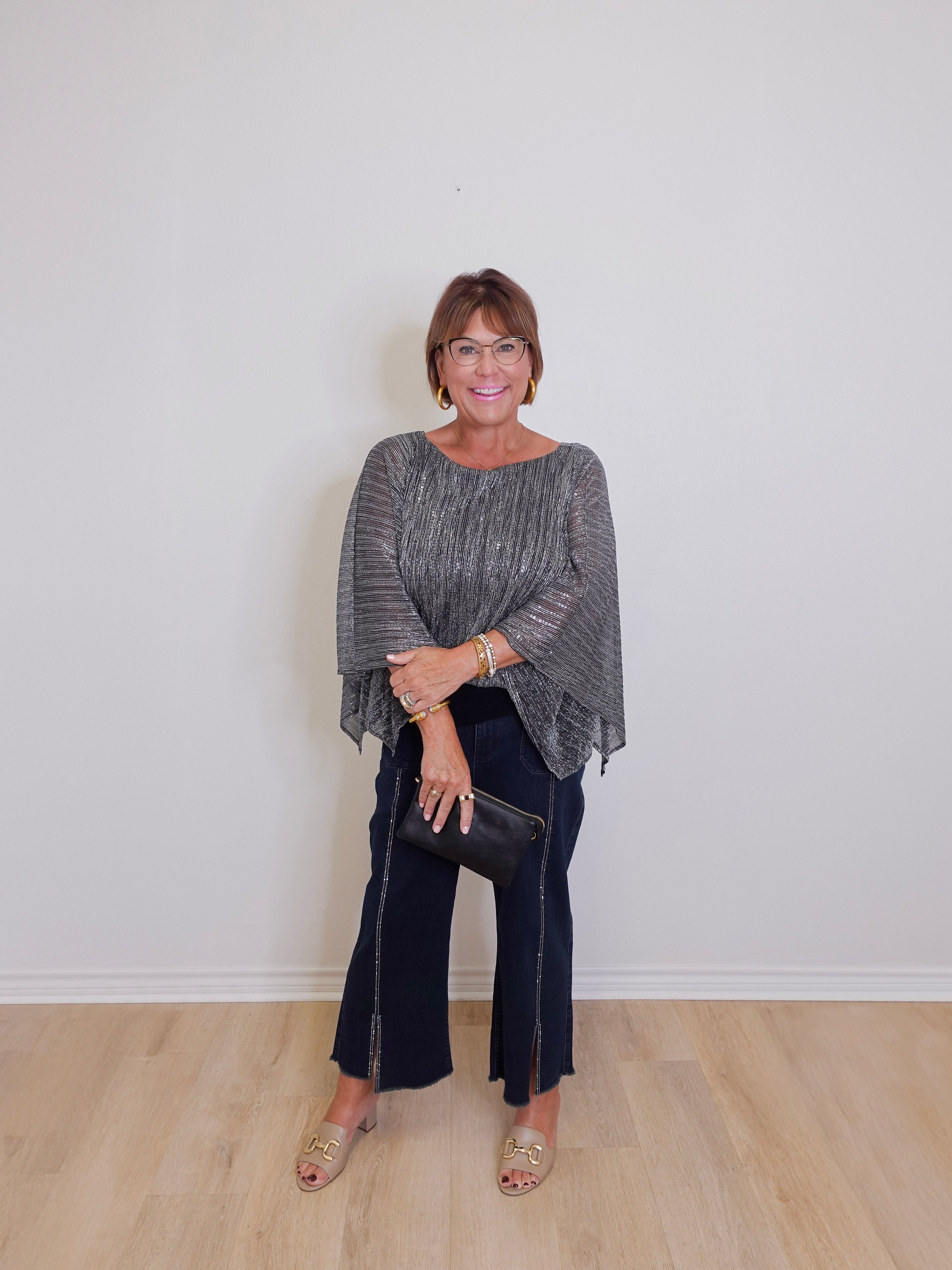 Woman wearing a gray sweater and black pants against a white wall.